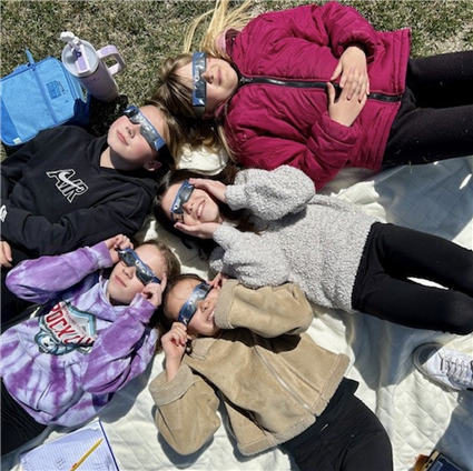 girls laying on grass looking up at the solar eclipse with eclipse glasses on 